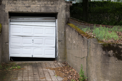 A garage door is broken and hanging in a worn down garage.
