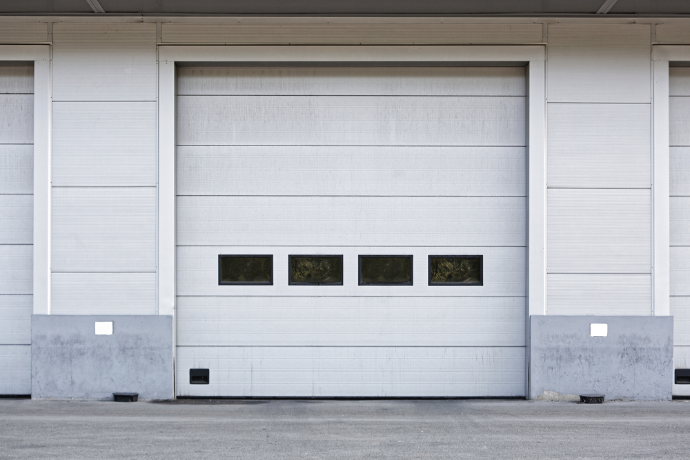 Technician inspecting commercial garage door safety sensors in an industrial facility